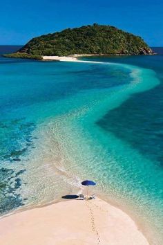 an aerial view of the beach and water in front of a small island with two umbrellas on it