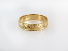 a gold wedding ring with an intricate design on the inside and outside, sitting on a white surface