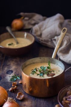 two bowls filled with soup on top of a wooden table next to onions and garlic