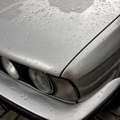 the front end of a silver car with rain drops on it