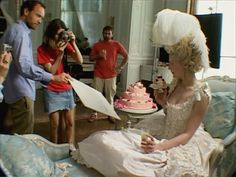 a woman in a wedding dress sitting on a bed next to a man taking pictures