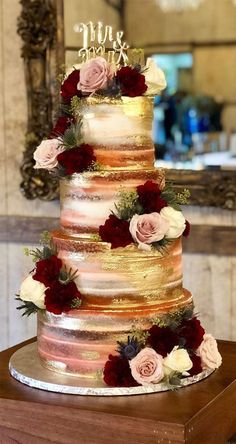 a multi layer wedding cake with flowers on the top and bottom tier, sitting on a table in front of a mirror