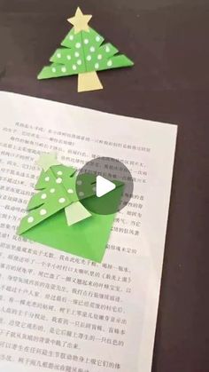 an origami christmas tree on top of a book with paper cut outs in the shape of trees