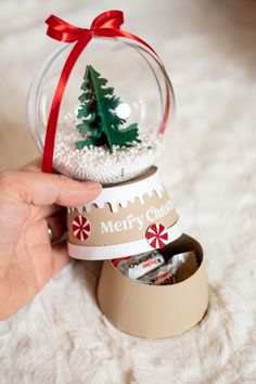 a hand holding a snow globe with a christmas tree inside it and candy in the bottom