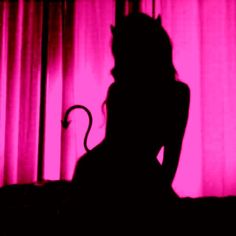 the silhouette of a woman sitting in front of a pink curtain