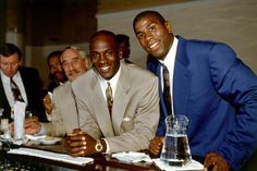 three men in suits are sitting at a bar smiling for the camera, while one man is holding a drink