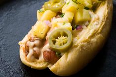 a hot dog with toppings on it sitting on a black plate, ready to be eaten