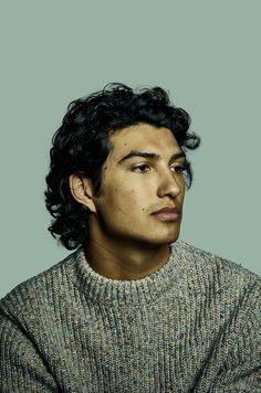 a young man with curly hair is looking off to the side while wearing a sweater