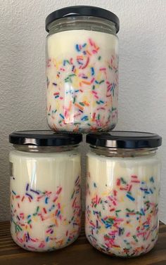 three jars filled with sprinkles on top of a wooden table