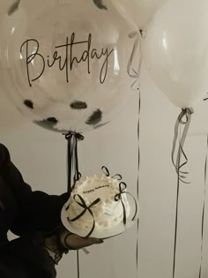 a person holding a cake and balloons with writing on the balloon says, happy birthday