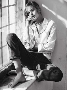 a woman sitting on the window sill with her hand to her mouth and looking out