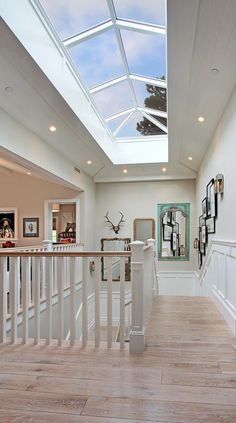 a hallway with white walls and wooden flooring has a skylight above the stairs