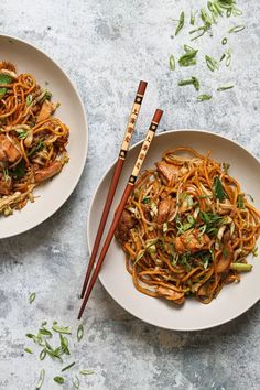 two white plates topped with noodles and meat next to chopsticks on a table