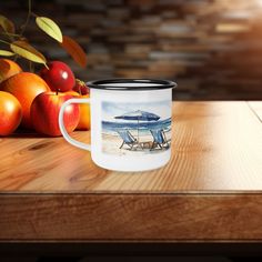 a coffee mug sitting on top of a wooden table next to apples and oranges