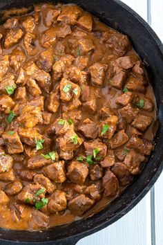 a skillet filled with meat and gravy on top of a wooden table