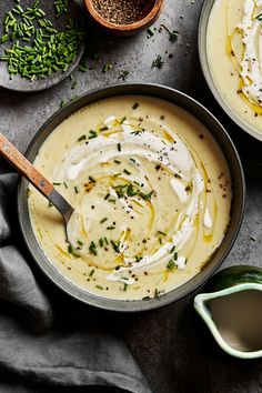 two bowls filled with cream and herbs on top of a gray table next to spoons