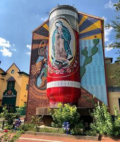 a large mural on the side of a building in front of trees and buildings with flowers