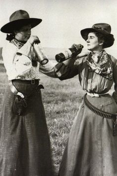 two women in long skirts and hats are holding bottles