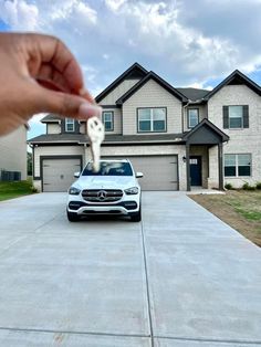 a hand is holding a key to a white mercedes suv parked in front of a house