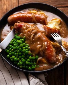 two sausages, peas and potatoes in a bowl with gravy on the side