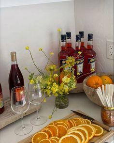 there are many oranges on the counter next to wine bottles and glasses with strawberries in them