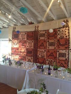 a room with many tables and chairs covered in white linens, decorated with colorful wall hangings