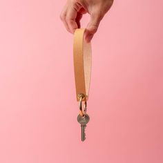 a hand holding a key on a pink background with a gold colored ribbon around it