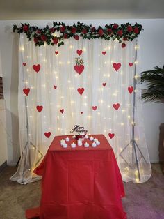 a red table topped with cupcakes next to a white curtain covered in lights