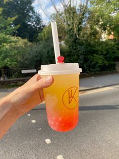 a person holding up a drink with a straw in it's hand on the street