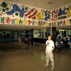 a man standing in front of a wall with graffiti on it's walls and people walking around