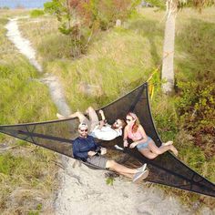 three people laying on top of a black kite in the middle of some grass and trees