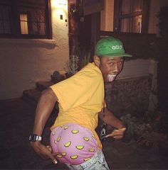 a man in yellow shirt and green hat on skateboard at night with building behind him