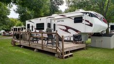 an rv parked in the grass next to a wooden deck