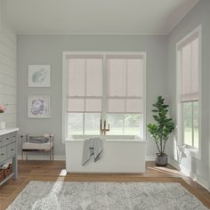 a bathroom with a tub, rug and two windows that have blind shades on them