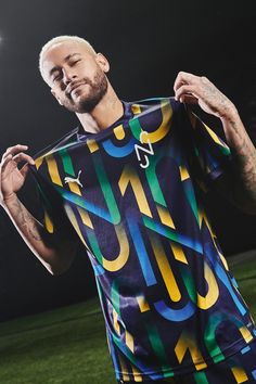 a man holding up a soccer jersey in front of a field at night with the lights on