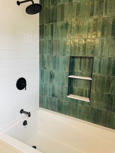 a bathtub with green tiles on the wall and shower head in the tub area