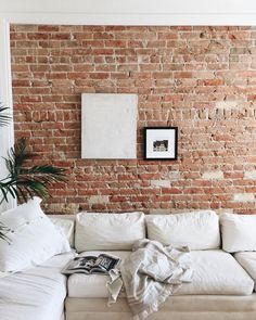 a white couch sitting in front of a brick wall next to a potted plant