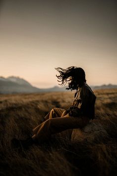 a man sitting in the middle of a field with his hair blowing in the wind