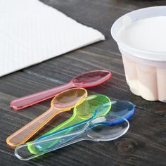 plastic spoons are lined up on a table next to a container of yogurt