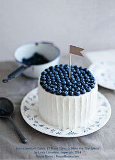 a white cake with blueberries on it and a flag sticking out of the top