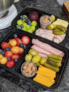 two black trays filled with different types of food on top of a counter next to a blender