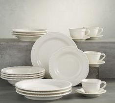 white dishes and cups are stacked up on a countertop in front of a gray background