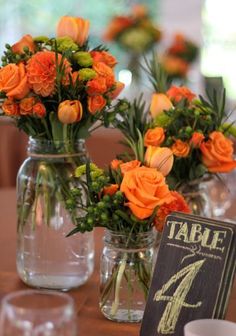 orange flowers in vases on a table with a sign and glass cups next to them