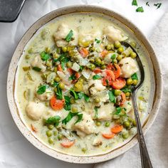 a bowl filled with chicken and vegetable soup on top of a white cloth next to a spoon