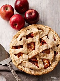 an apple pie on a wooden table next to three apples