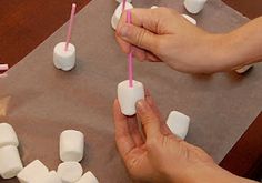 two hands holding toothbrushes over marshmallows on a table