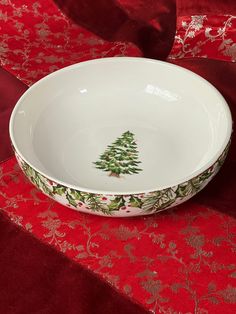 a white bowl with a christmas tree painted on the side sitting on a red table cloth