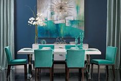 a dining room table with blue chairs and a painting hanging on the wall behind it