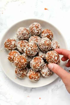 a hand is picking up some powdered sugar balls on a white plate