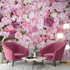 two pink chairs sitting in front of a wall with flowers on it and a coffee table